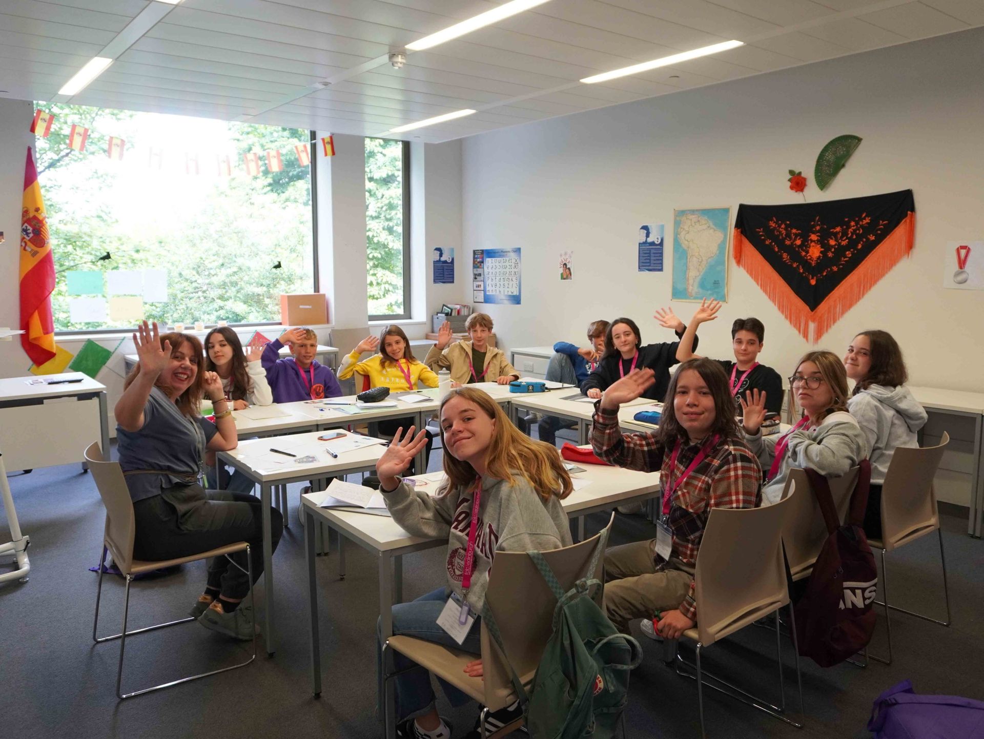 Image of 11 students and one teacher around a row of tables waving at the camera