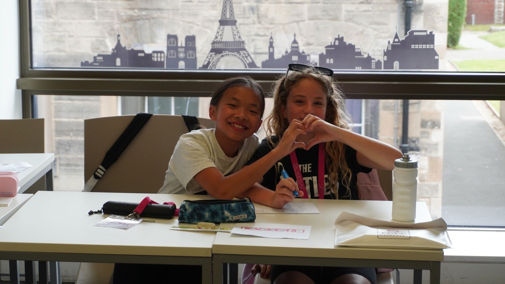 Two students making a love heart with their hands in class