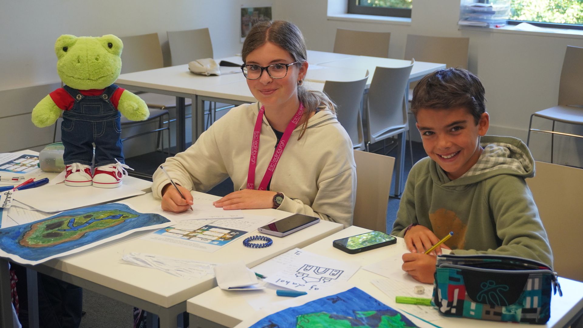 Two students smiling at the camera with a green teddy off to the left of the frame