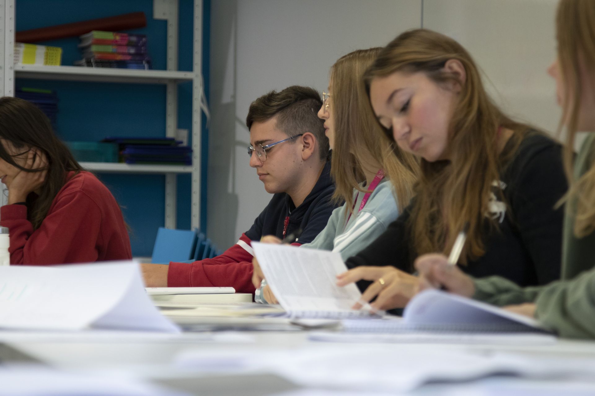 Image of out of focus students with one student in focus. All students working on something in class