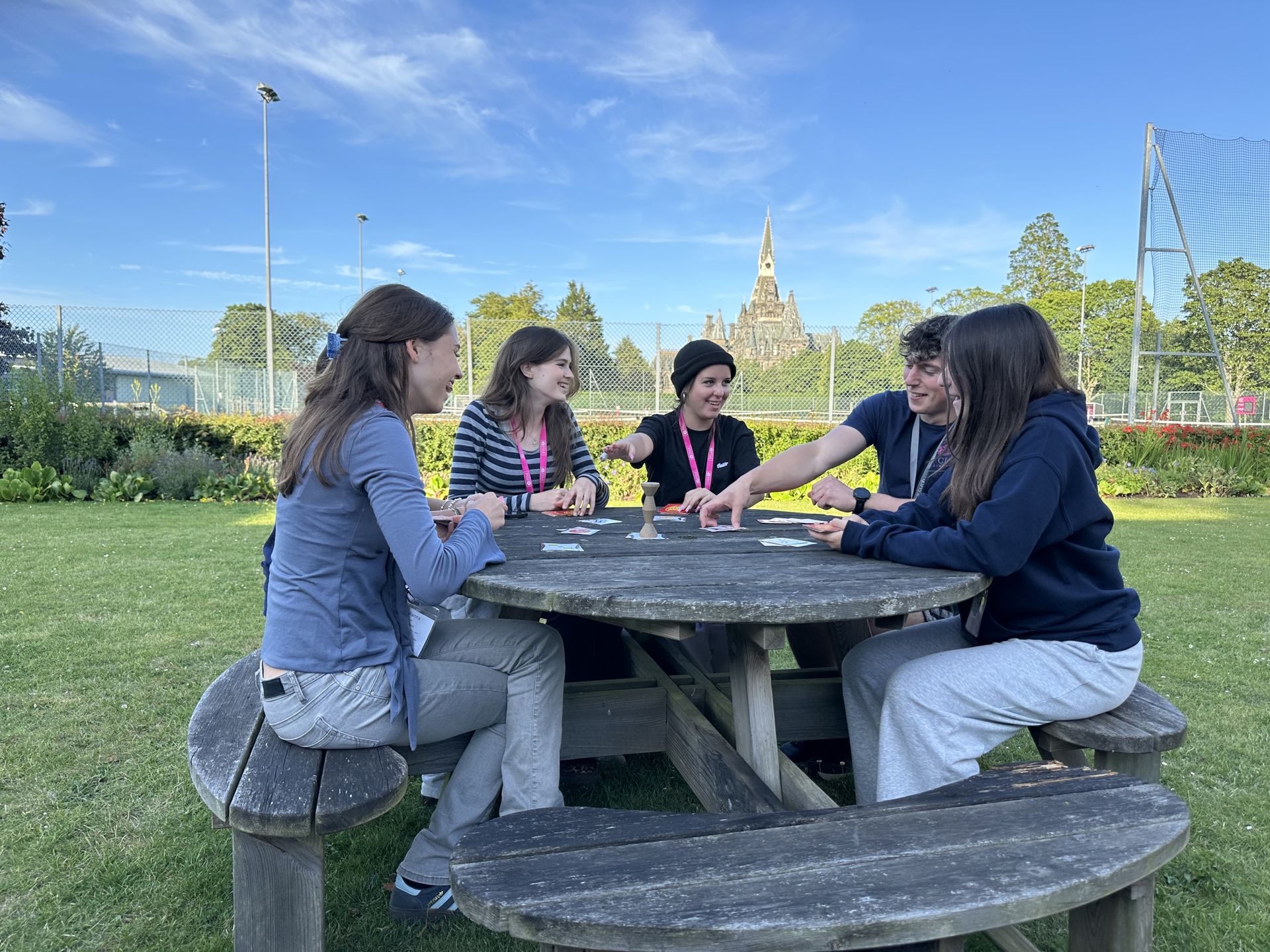 Shows students and staff playing a card game with the main building in the background
