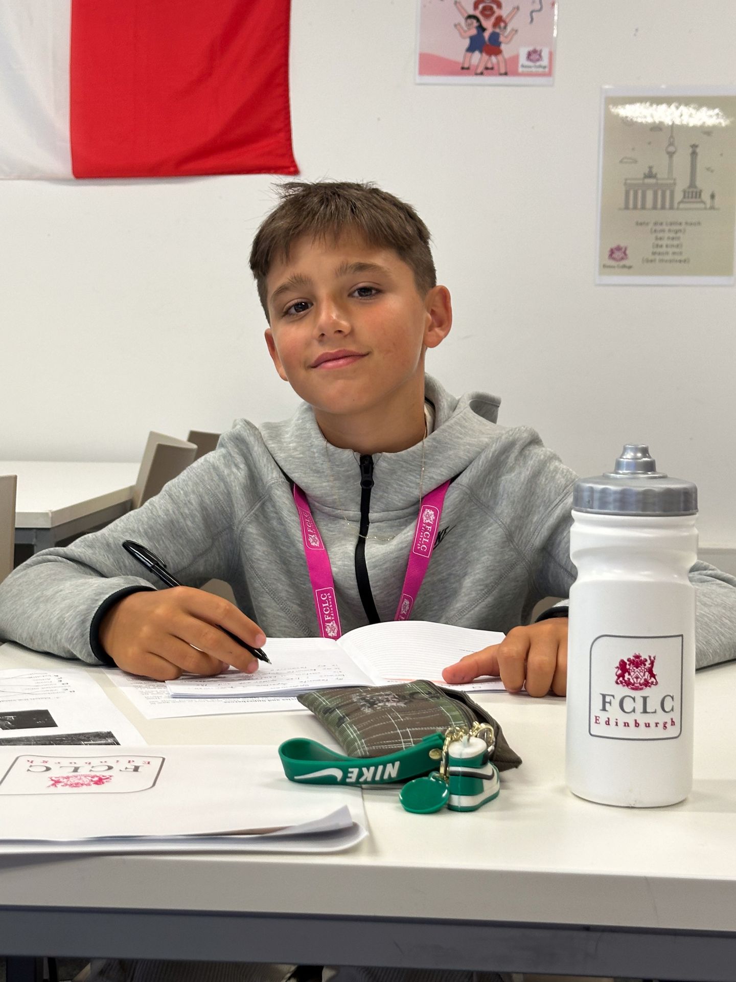 Image of student smiling at the camera whilst working. FCLC logo on water bottle at front right of frame